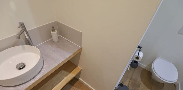 Ein Badezimmer mit Waschbecken, Toilette und einem kleinen Ablagefach.