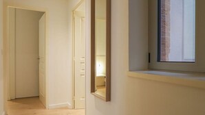 A hallway with a door leading to a room, a window with a view of a brick wall, and a mirror on the wall.
