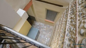 A narrow hallway with a small window, patterned floor tiles, and a stone wall.