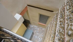 A narrow hallway with a small window, patterned floor tiles, and a stone wall.