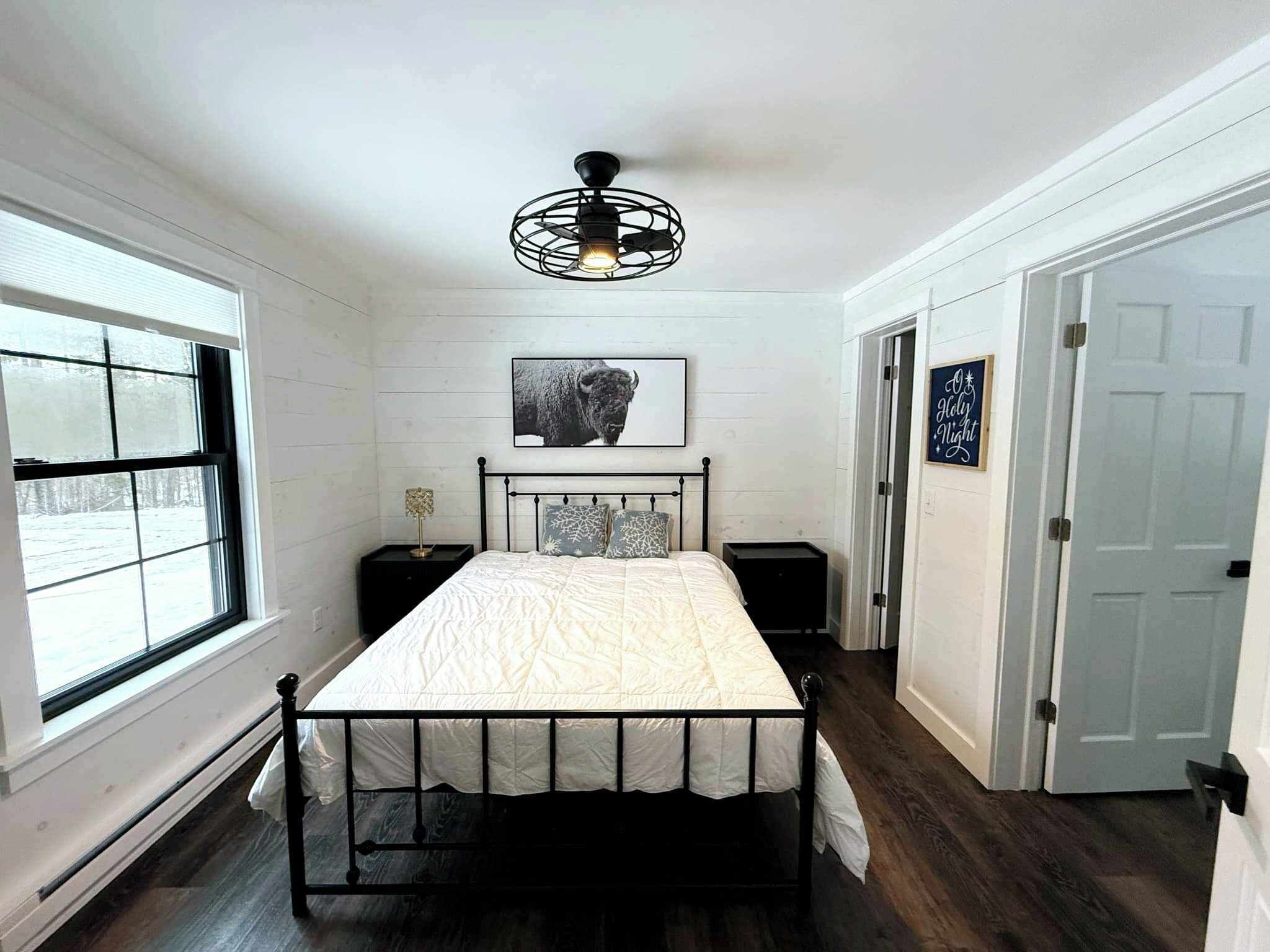 A bedroom with a bed, a ceiling fan, a window, and a door.