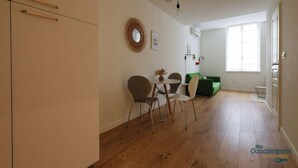 A modern living room with a dining area, wooden flooring, a green sofa, and a dining table with chairs.