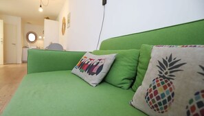 Um sofá verde com almofadas coloridas e uma almofada com desenho de abacaxi.