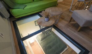 Una sala de estar moderna con un sofá verde, una mesa de centro redonda de madera con un florero y un sillón gris.
