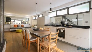 Une cuisine moderne dotée d’un îlot central, de meubles blancs et d’un coin repas avec des chaises en bois et une table foncée.