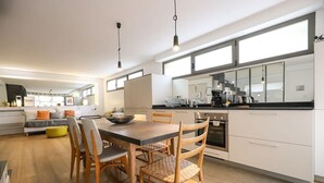 Une cuisine moderne avec des meubles blancs, une table à manger avec des chaises et une grande fenêtre qui laisse entrer la lumière naturelle.