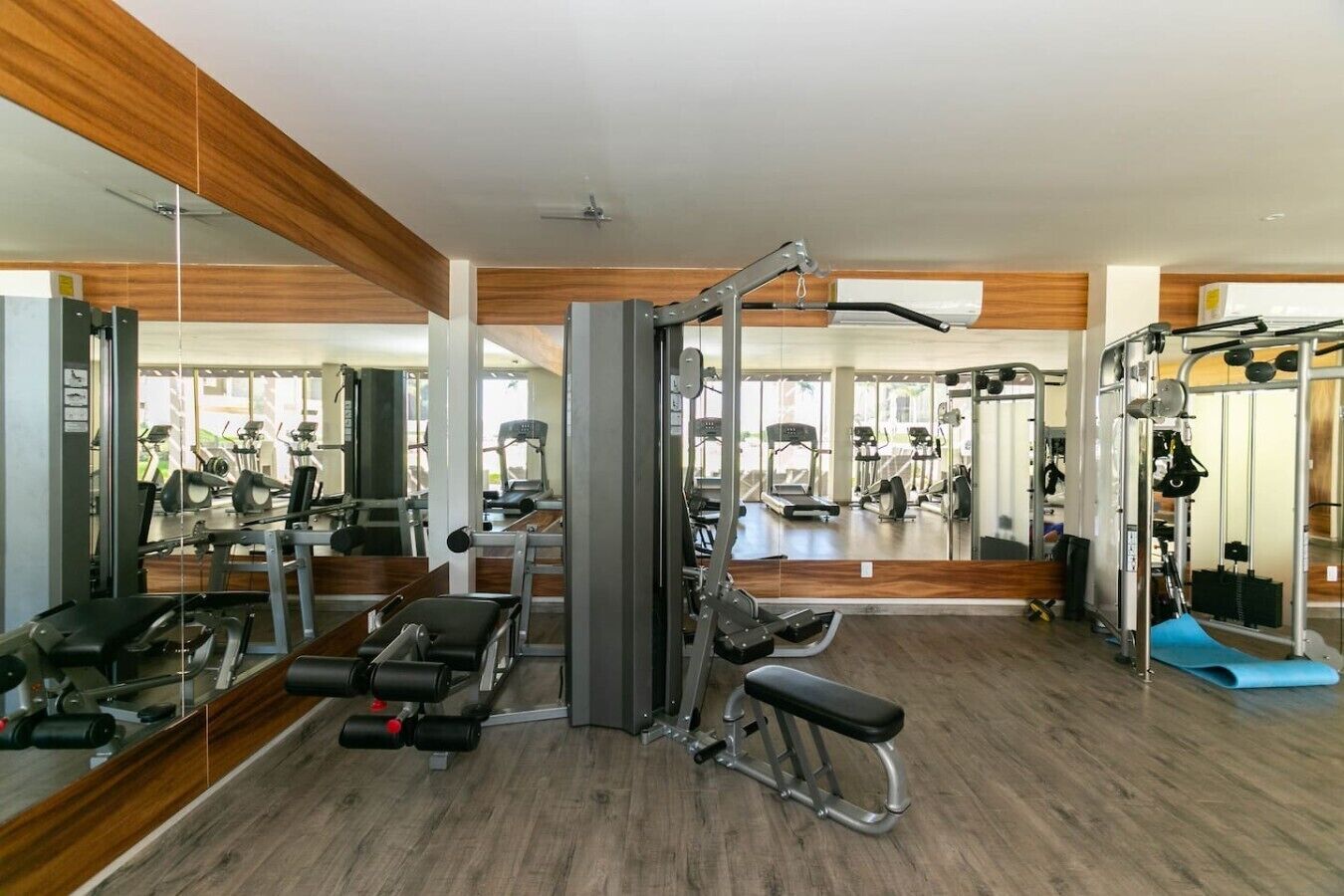 Ein Fitnessstudio mit unterschiedlichen Trainingsgeräten, Spiegeln und einem Holzboden.