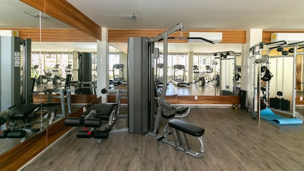 A gym with various exercise equipment, mirrors, and a wooden floor.