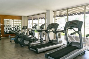 A gym with multiple treadmills and stationary bikes, large windows, and a wooden floor.