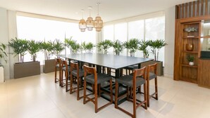 A modern dining area with a long table, multiple chairs, and pendant lighting.