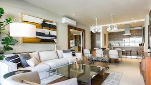 A modern living room with a glass coffee table, a sofa, and a dining area with chairs.