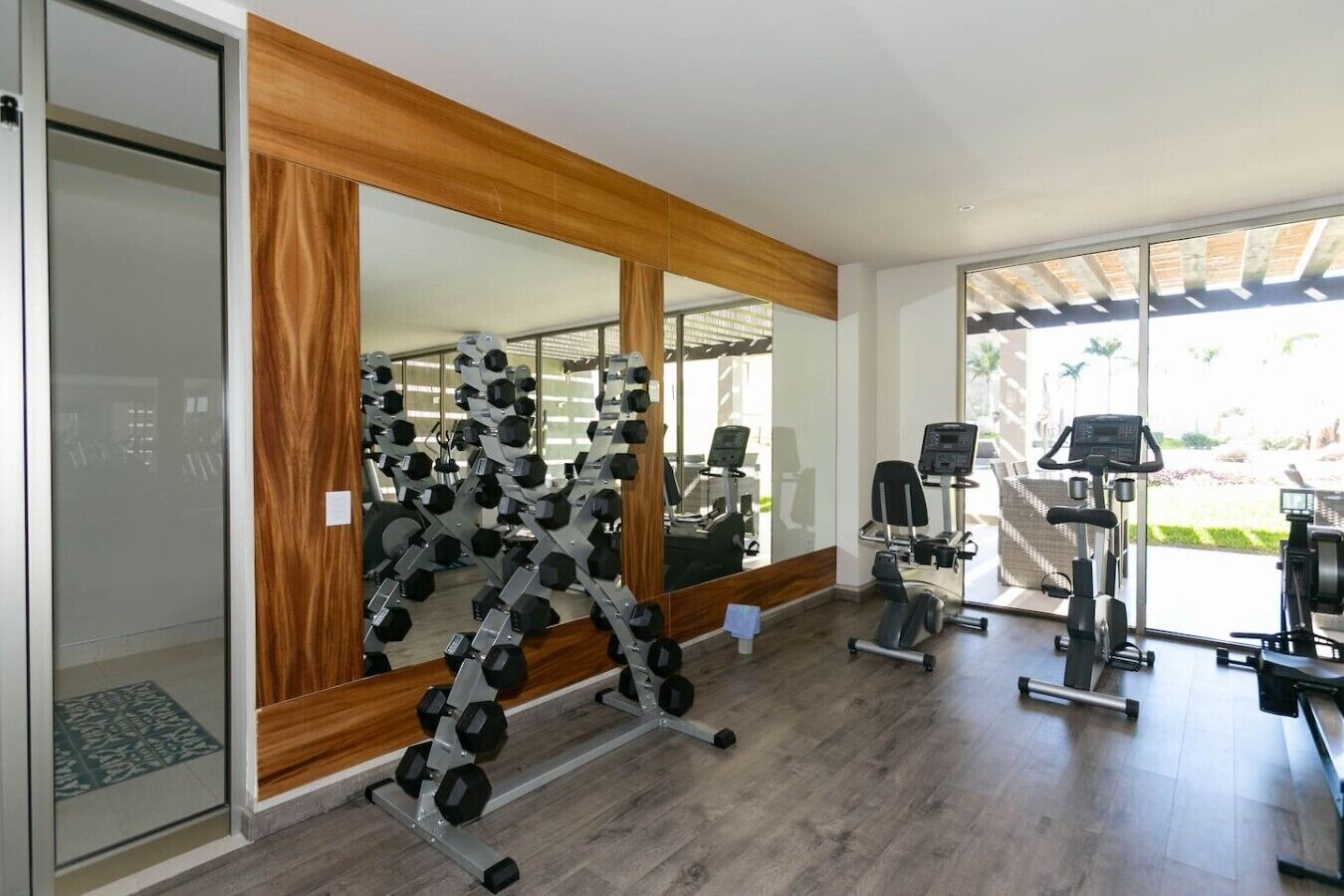 Ein Fitnessraum mit Trainingsgeräten, einem großen Spiegel und Blick ins Freie.