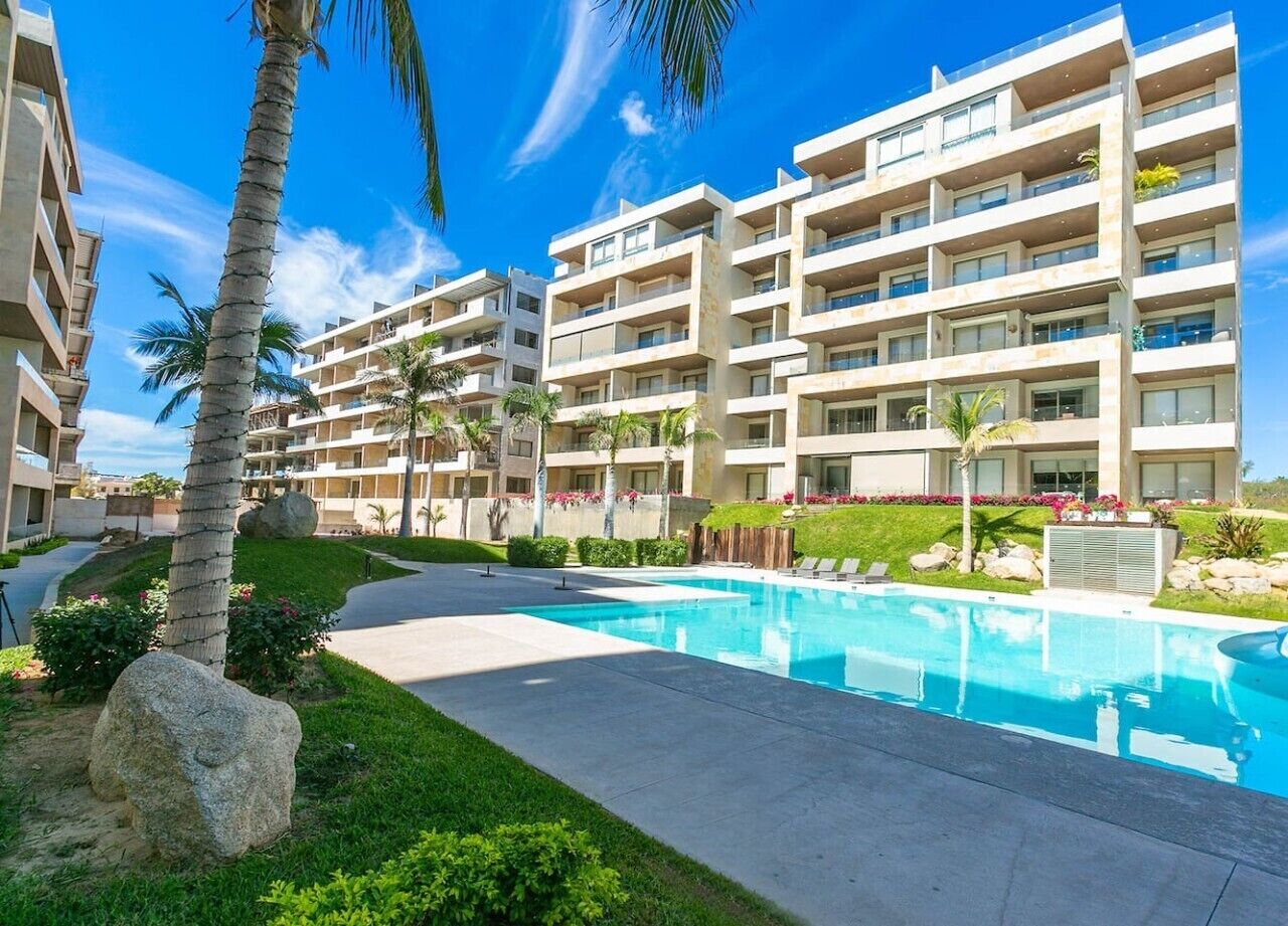 A resort with a swimming pool, multiple-story buildings, and palm trees.