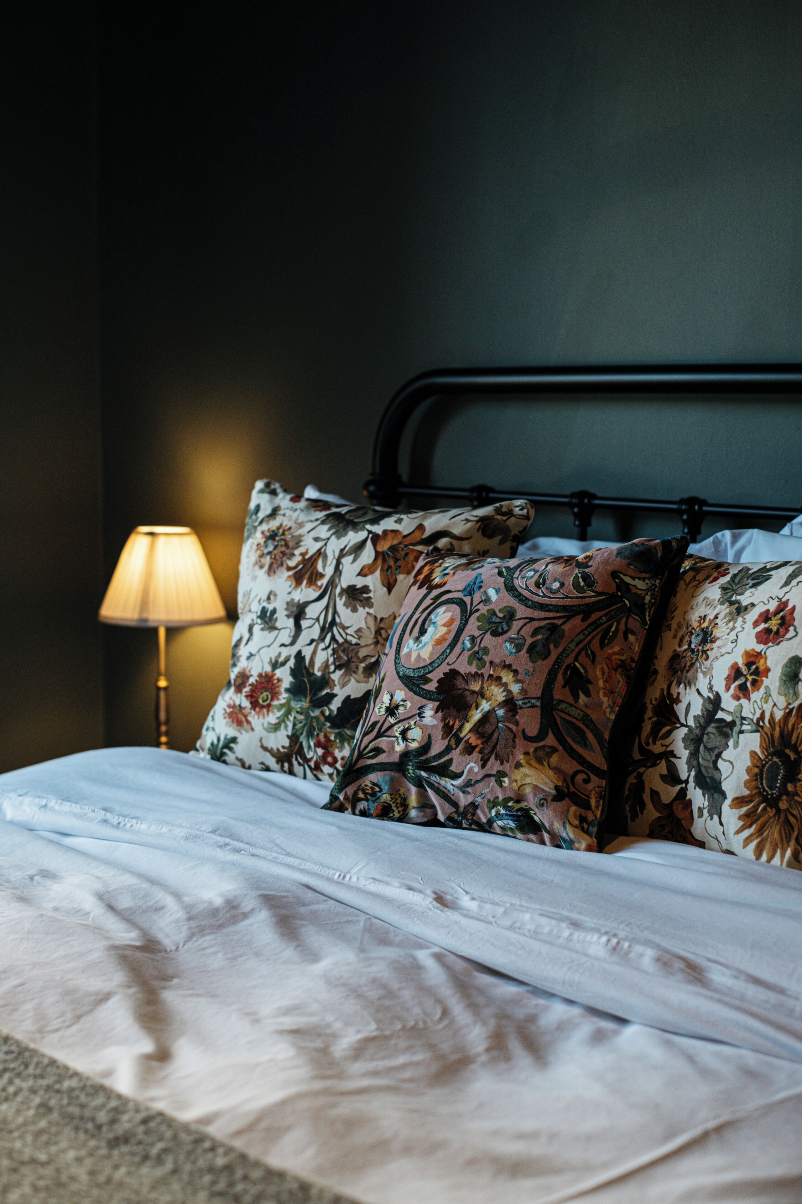 A neatly made bed with floral-patterned pillows and a bedside lamp.