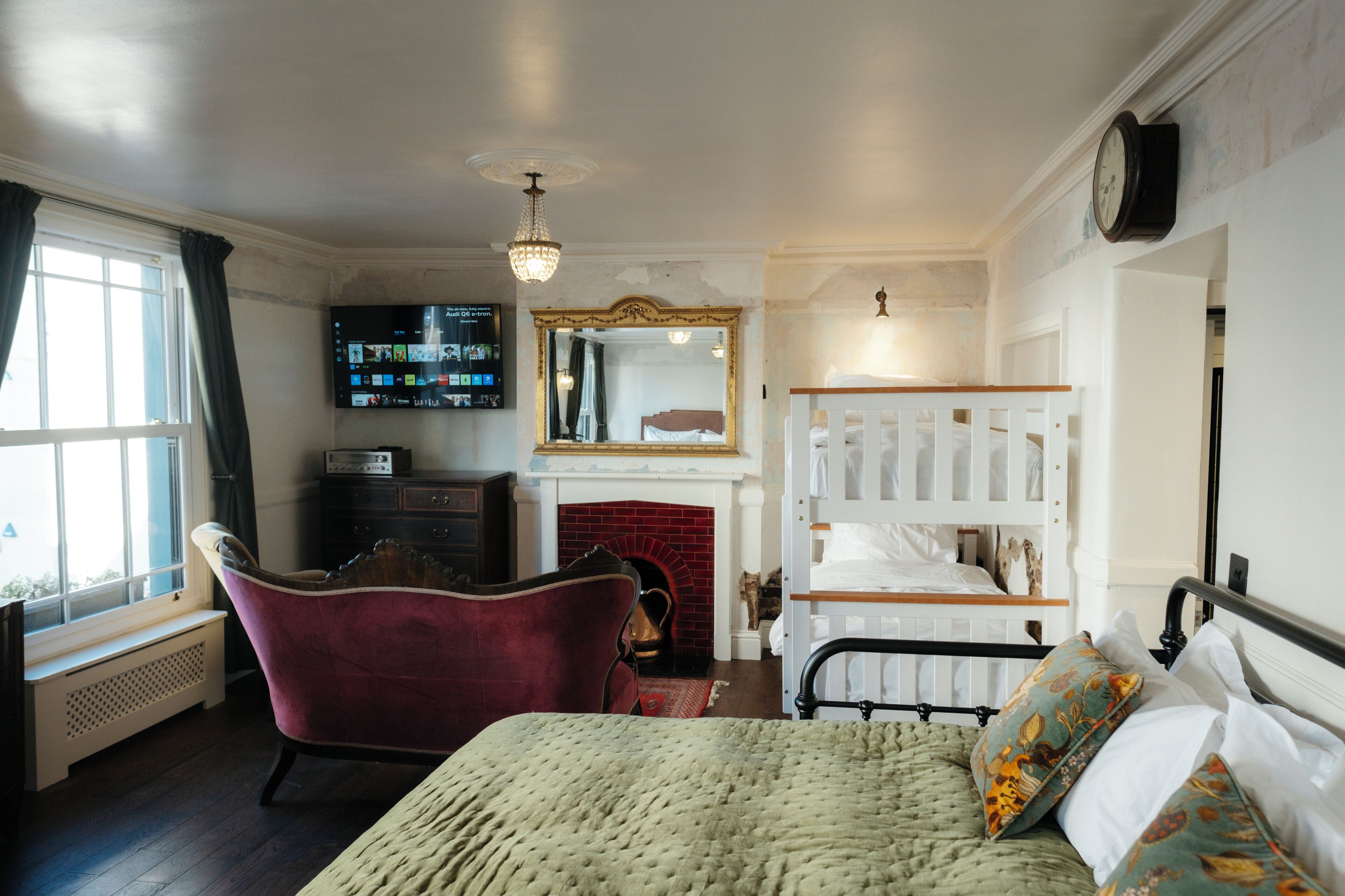 A bedroom with a bed, a red armchair, a fireplace, a television, and a mirror.