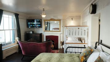 A bedroom with a bed, a red armchair, a fireplace, a television, and a mirror.