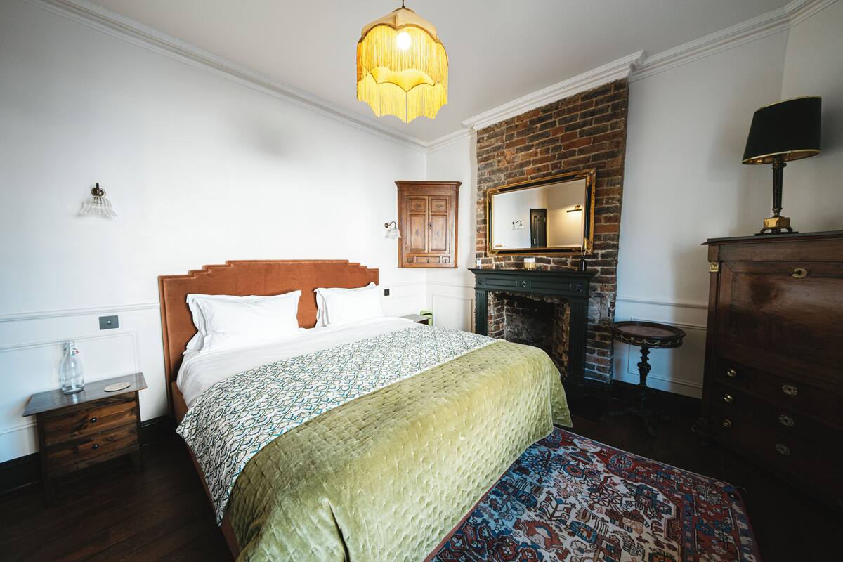 A bedroom with a bed, a wooden nightstand, a dresser, a mirror, and a fireplace.