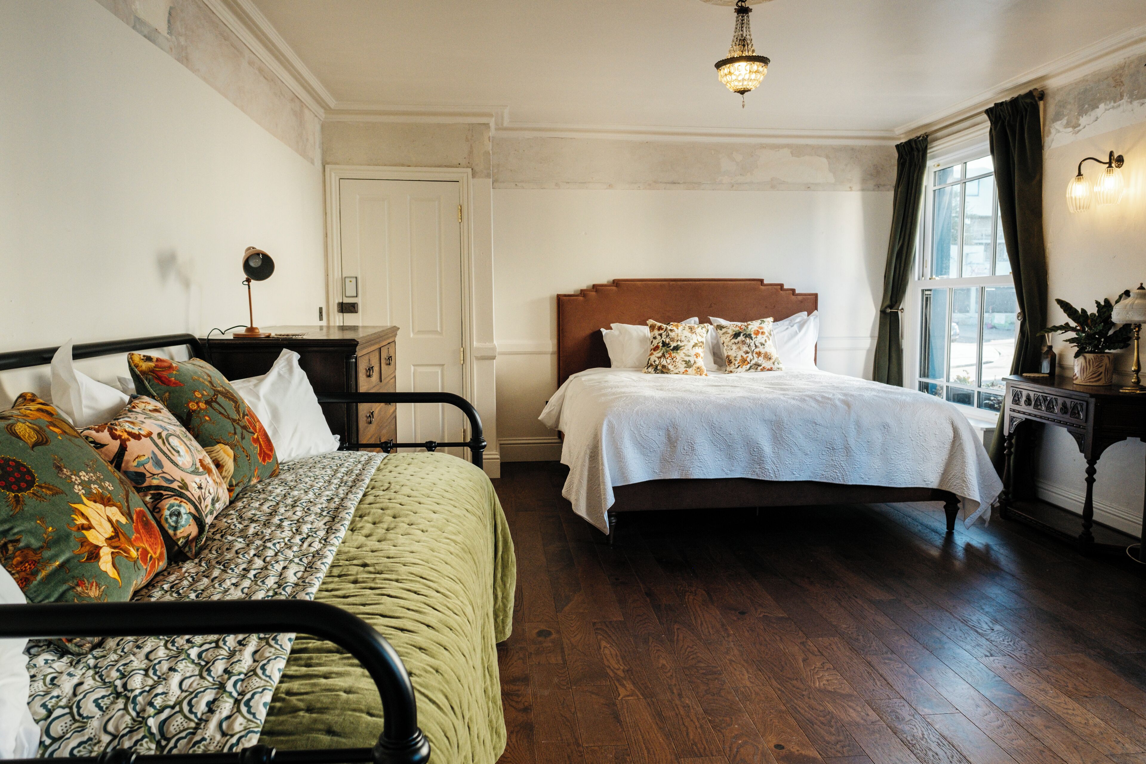 A bedroom with a bed, a bedside table, a lamp, a window with curtains, and a door.