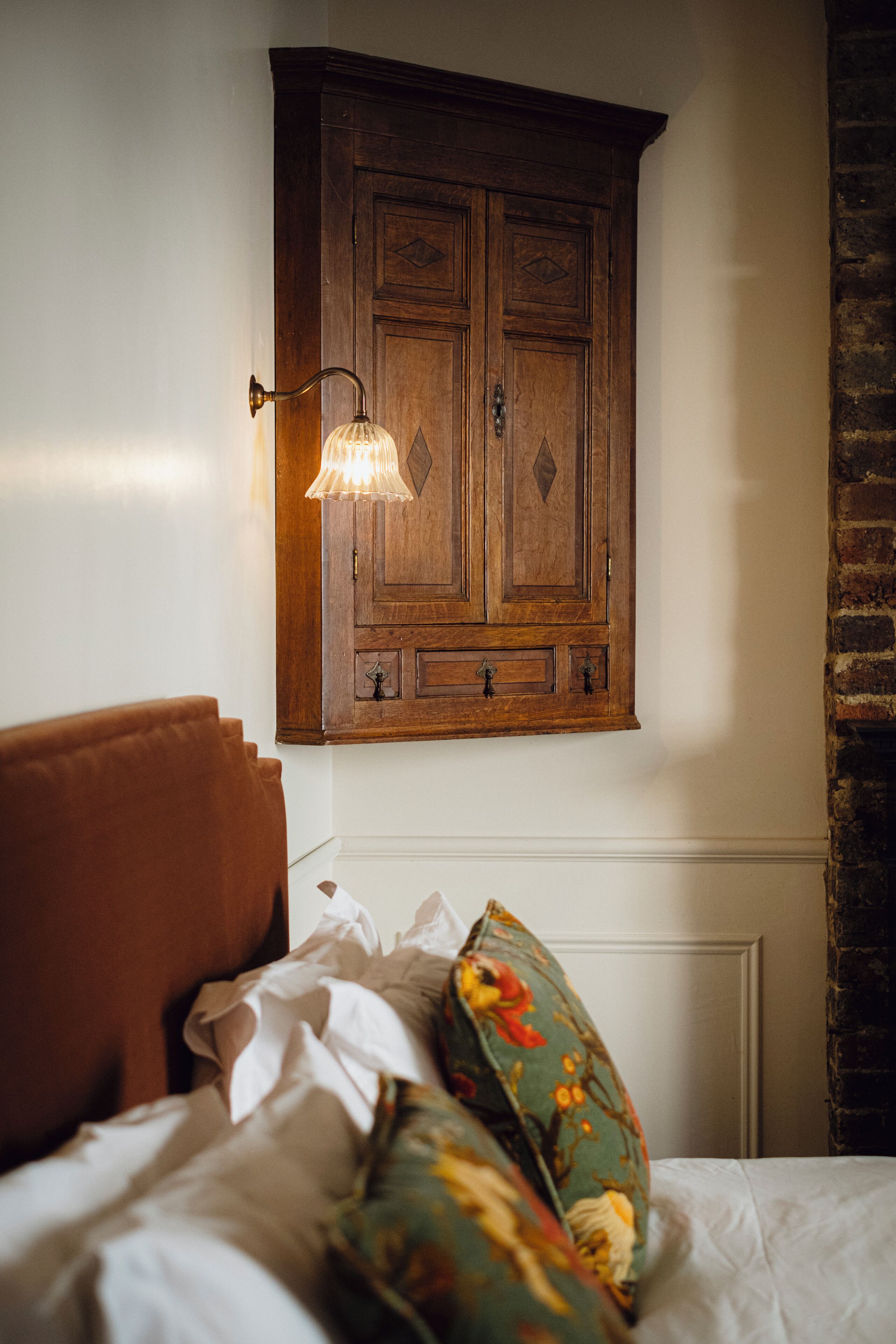 A bedroom with a wooden wardrobe, a bed with floral pillows, and a wall-mounted light fixture.