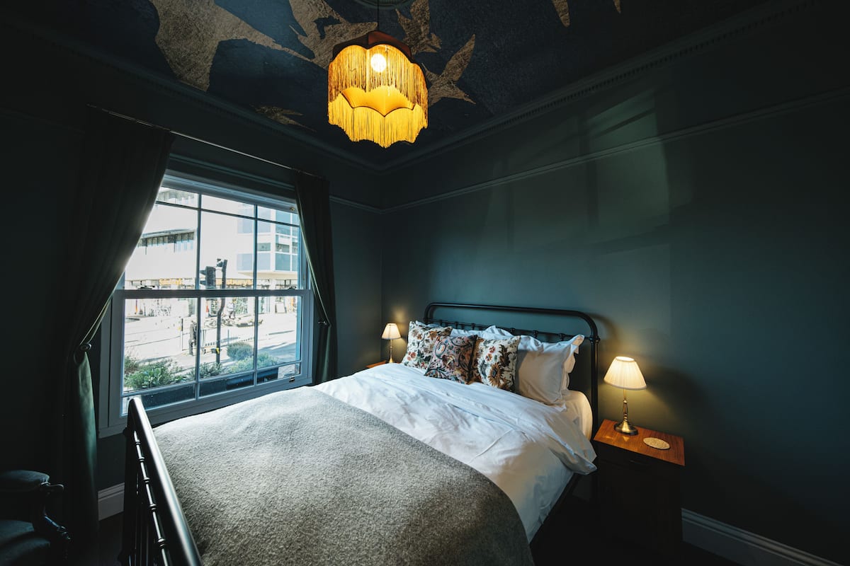 A hotel room with a large bed, two bedside lamps, a window with a view of the street, and a decorative ceiling light.