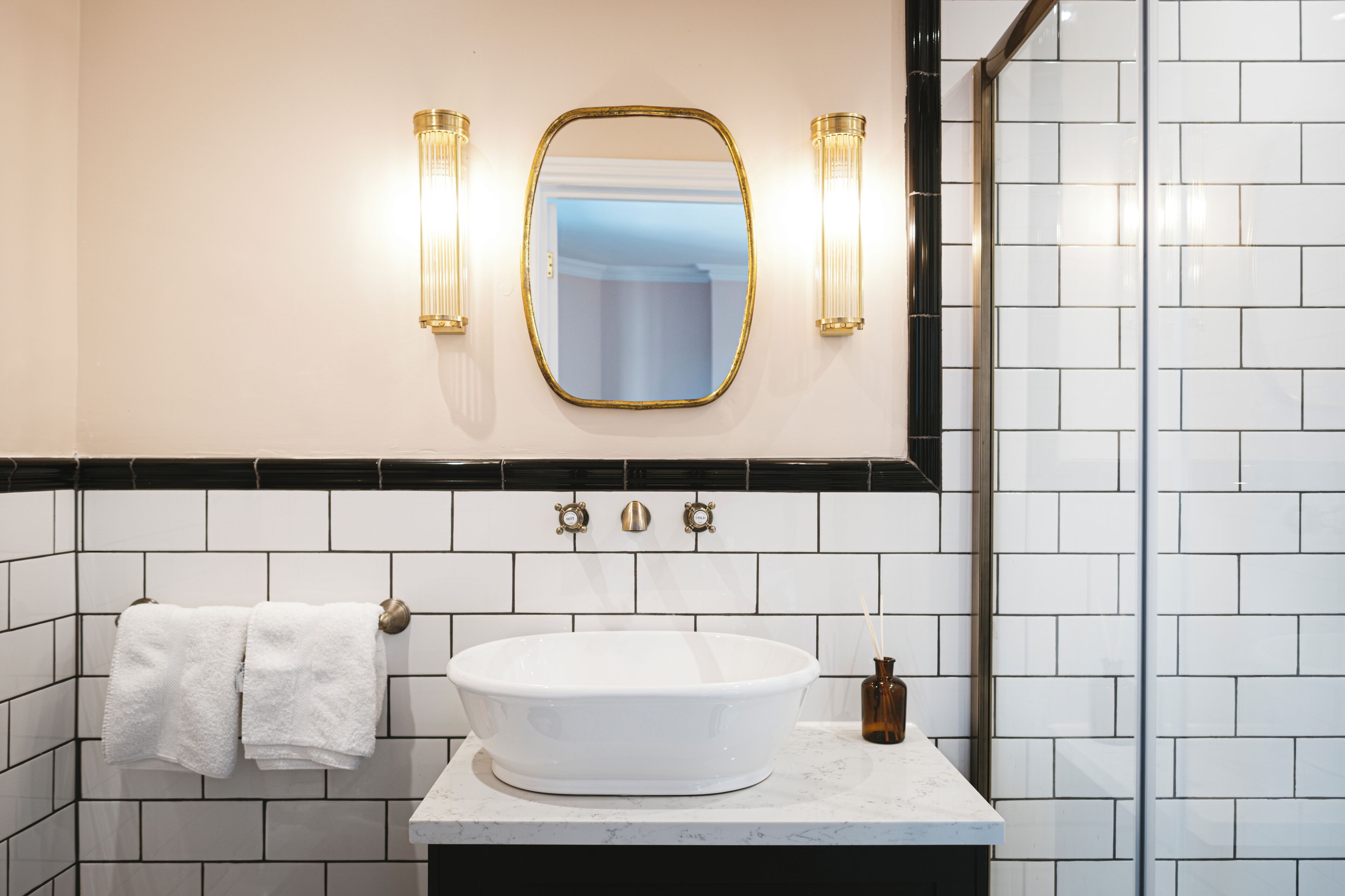 A bathroom with a white sink, a mirror with a gold frame, and two wall-mounted lights.