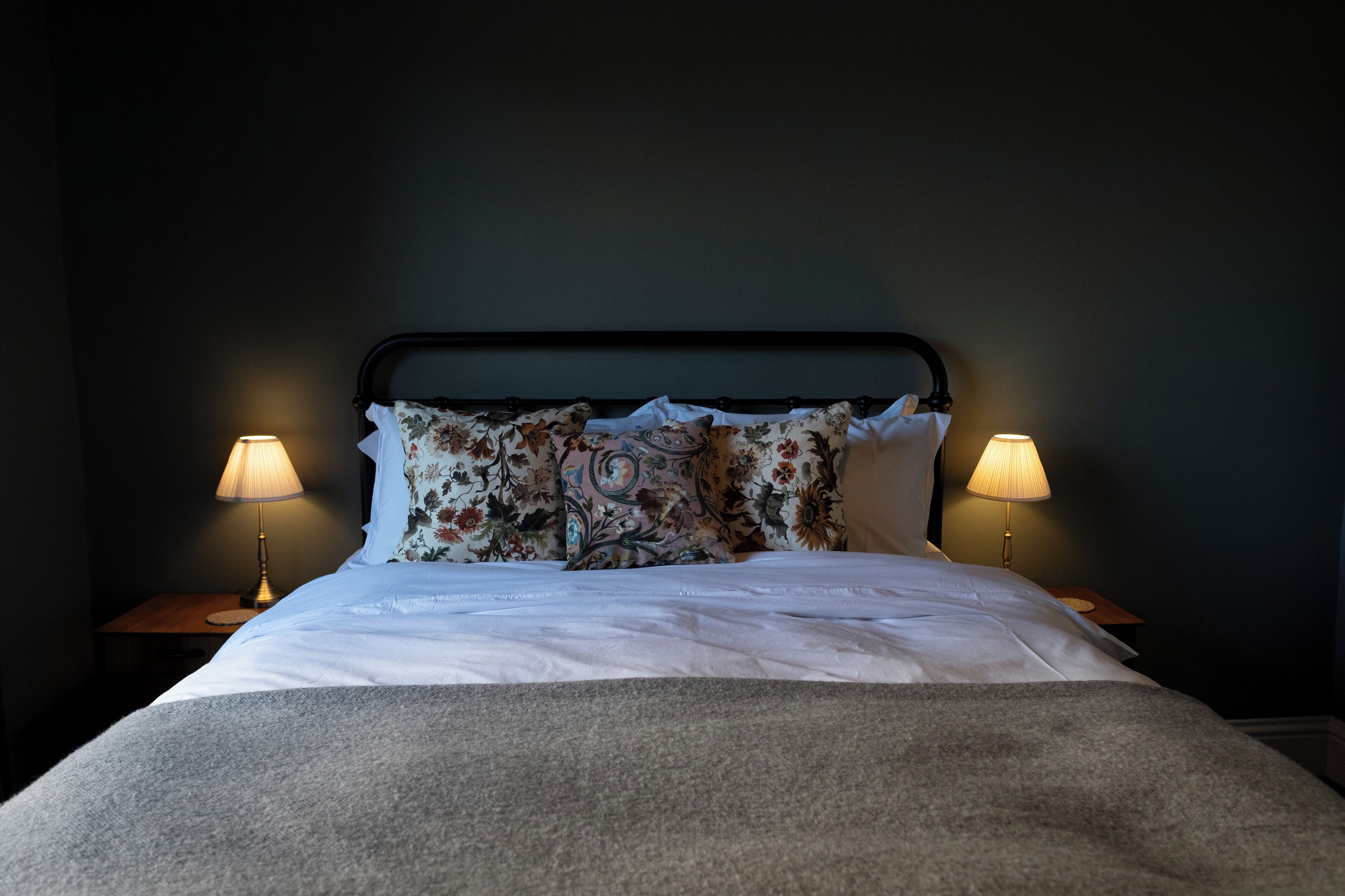 A neatly made bed with floral pillows and two bedside lamps.