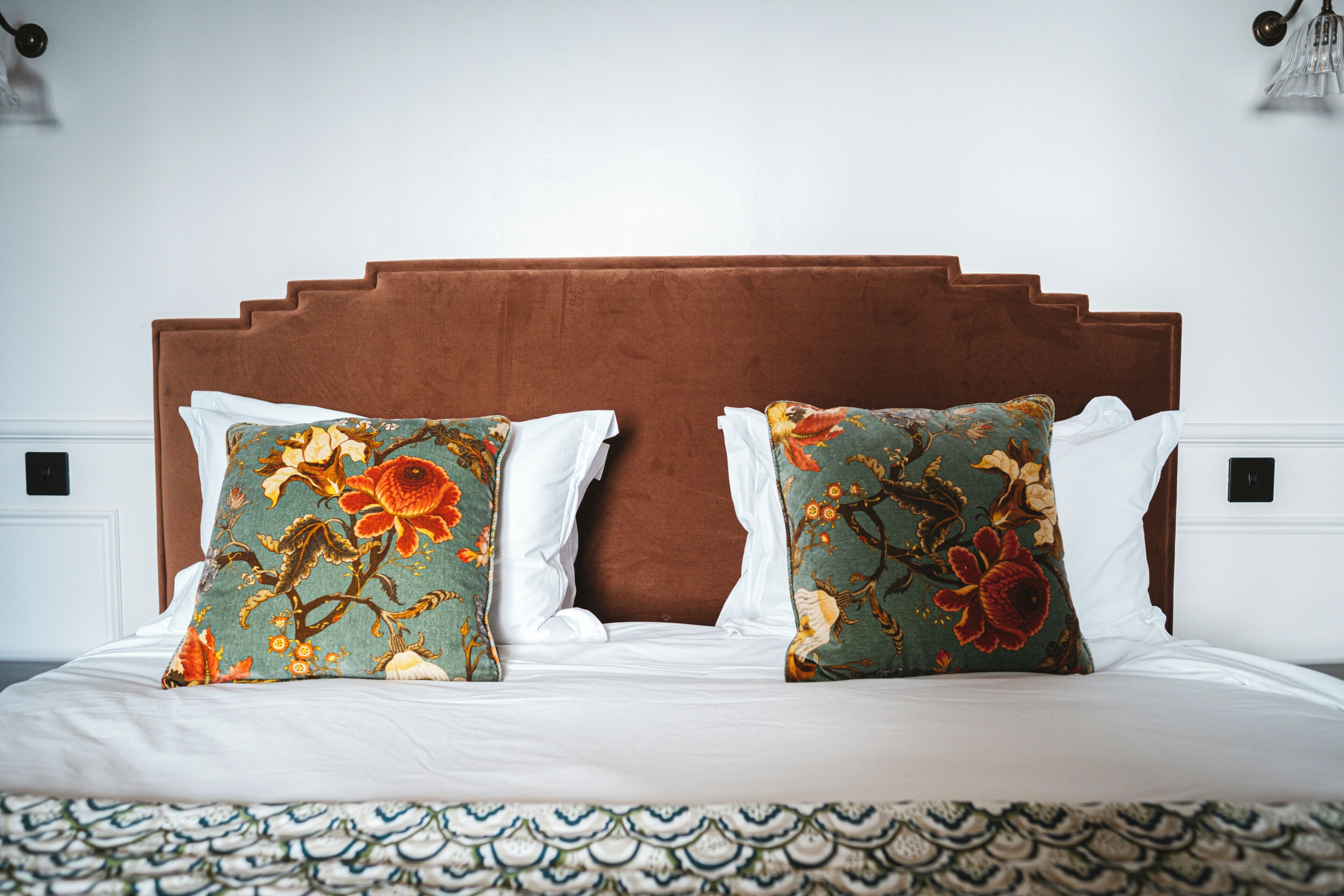 A bed with a brown headboard, two decorative pillows, and a patterned bedspread.