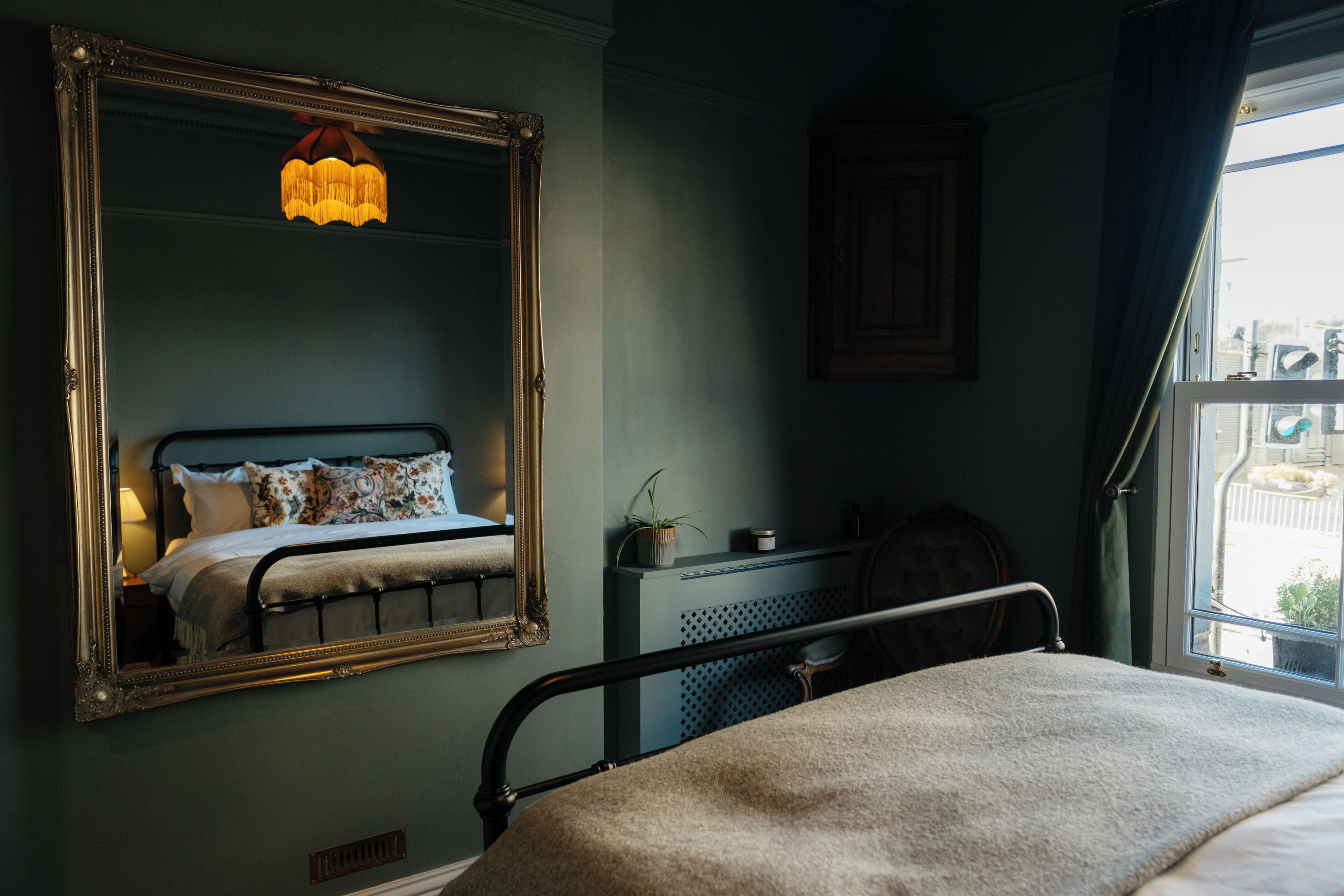 A bedroom with a large mirror, a bed with a headboard, a bedside table, a nightstand, a dresser, and a window with curtains.