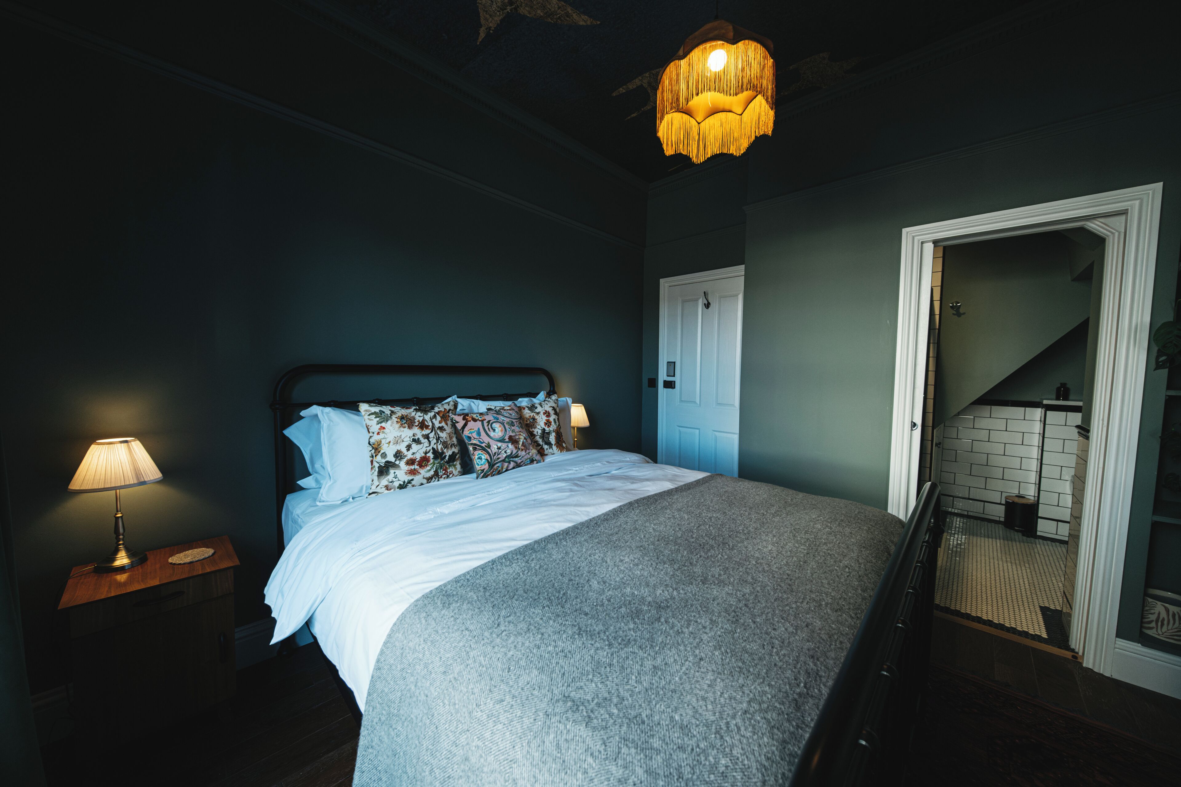 A bedroom with a bed, a nightstand with a lamp, a door, and a staircase.