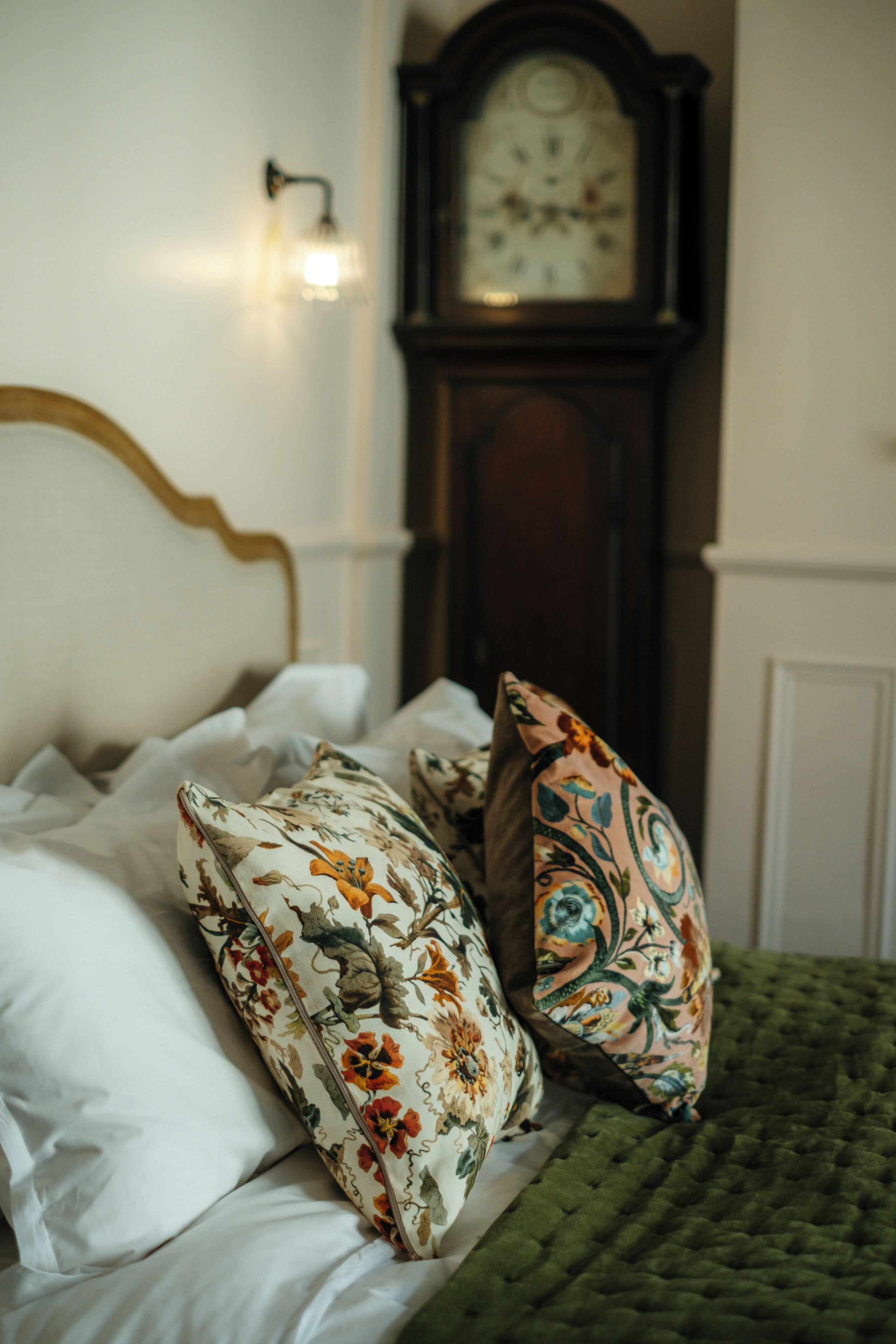 Una cama con almohadas de estampado floral, colcha verde y cabecera de madera.