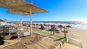 Un resort sulla spiaggia con zone solarium in legno, ombrelloni di paglia e comode poltrone da relax.