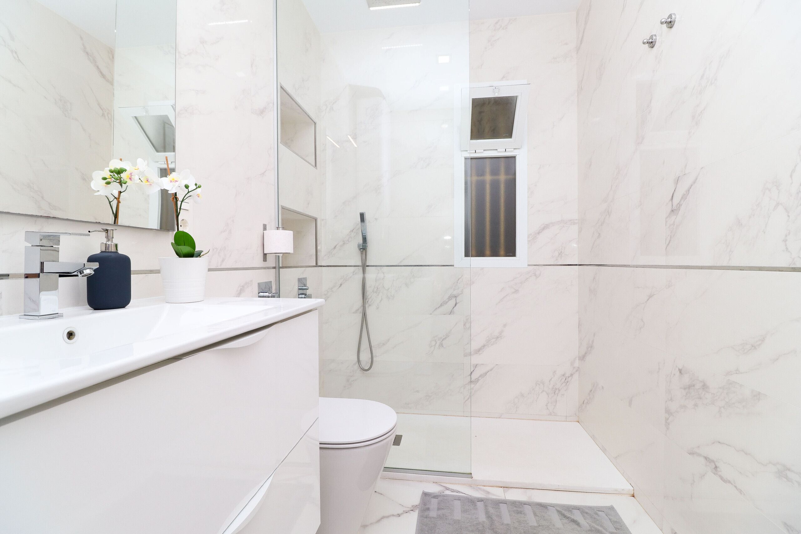 Een moderne badkamer met een wit marmeren wastafel, toilet en douche.