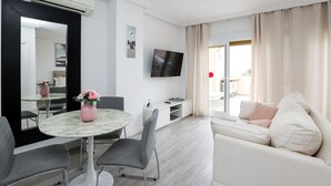 Un soggiorno moderno con un tavolo rotondo, sedie grigie, un divano bianco e una TV montata a parete.