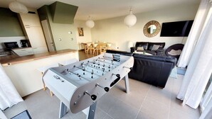 A modern living room with a foosball table, a dining area, a sofa, and a TV. - Modern villa 3 bedrooms with garden, WiFi and parking, close to beach (Wimereux)