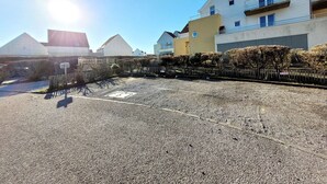 A parking lot with a gravel surface, a metal fence, and a row of houses with a clear sky and sunlight. - Modern villa 3 bedrooms with garden, WiFi and parking, close to beach (Wimereux)