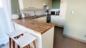 A modern kitchen with a wooden countertop, white cabinets, and a small dining area with a white table and chairs. - Modern villa 3 bedrooms with garden, WiFi and parking, close to beach (Wimereux)