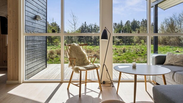A modern interior with a large window, wooden flooring, a rocking chair, a table, and a sofa. - Modern holiday home from 2017, located at Lild Strand. (Frøstrup)