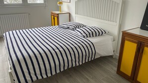 A neatly made bed with striped bedding, a white headboard, and a bedside table with a lamp.