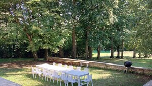 An outdoor dining area with a long table and chairs, surrounded by trees.