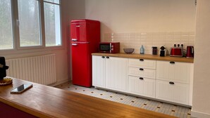 A kitchen with a red refrigerator, white cabinets, a wooden countertop, and a window with a view of trees.