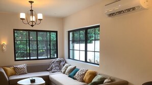 Una sala de estar moderna con un sofá modular, una mesita redonda y dos ventanas amplias que dan a vistas de vegetación.