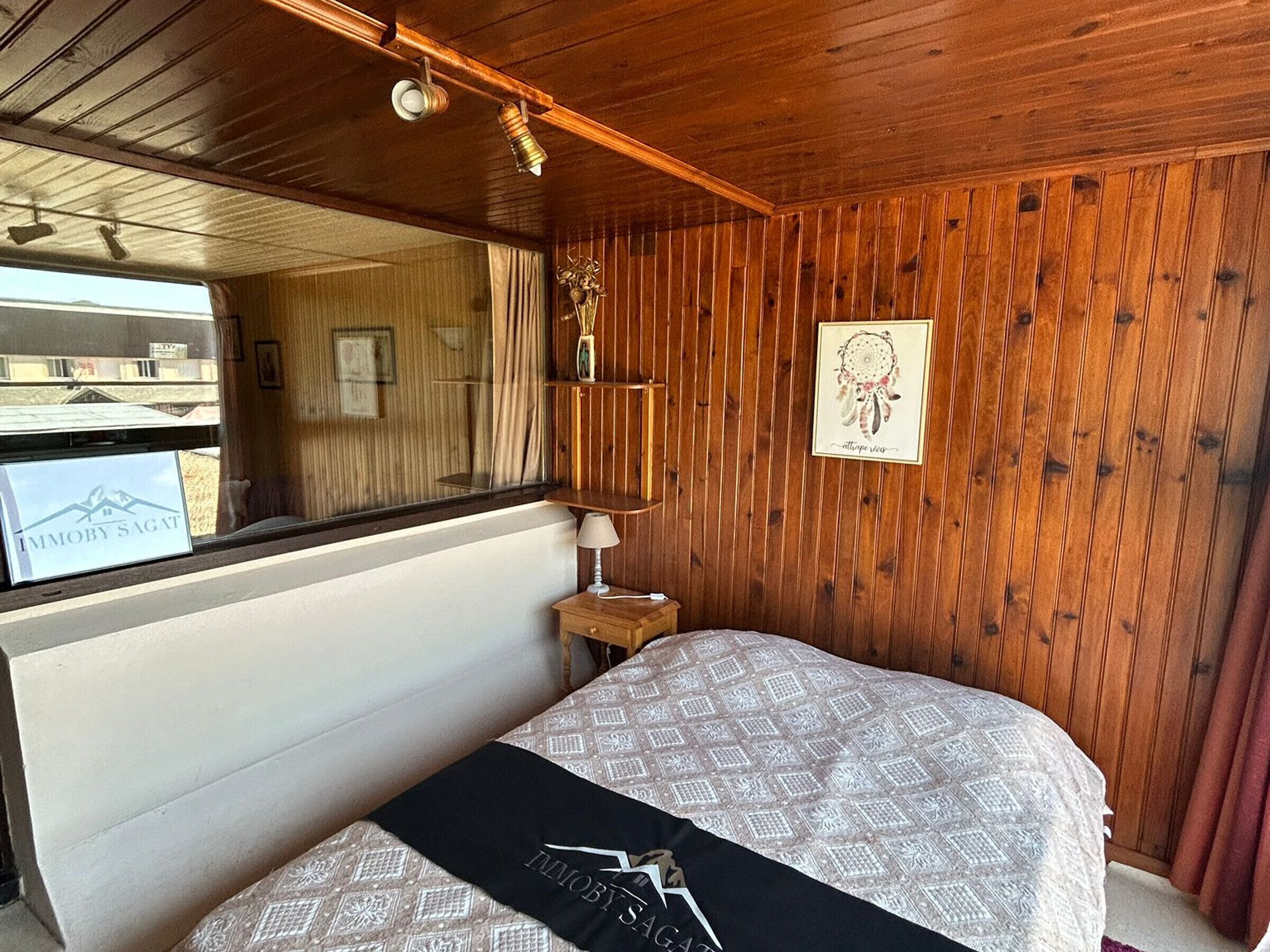A wooden-paneled room with a bed, a nightstand, a mirror, and a dreamcatcher on the wall.
