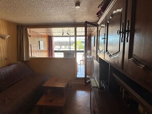 Ein Zimmer mit Holzbalkendecke, einer Couch, einem kleinen Tisch und einem Schrank mit Spiegel.
