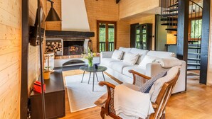 Un interior de cabaña acogedor con chimenea, paredes de madera, un sofá blanco y un comedor.