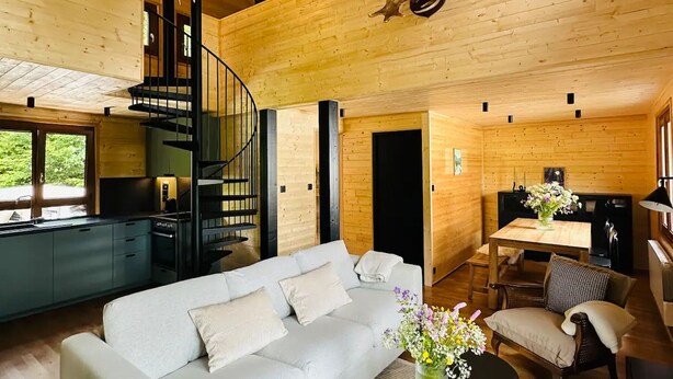 Interior moderno de una cabaña de troncos con un sofá blanco, un comedor y una escalera de caracol.