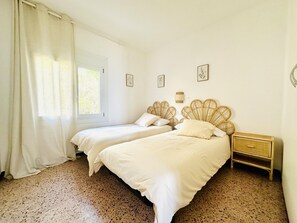 A bedroom with two beds, a window with curtains, a bedside table, and wall-mounted artwork.