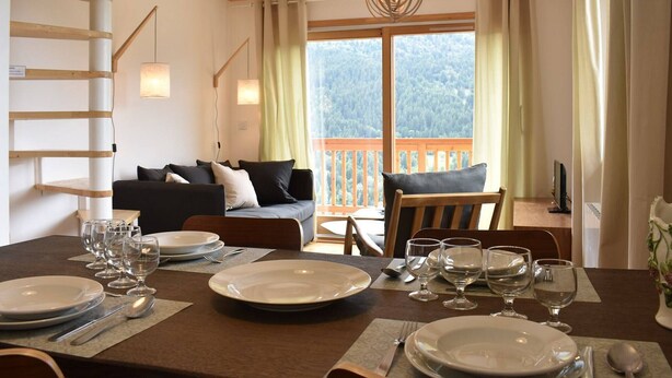 A dining area with a table set for four, a sofa, and a view of a forested landscape through large windows. - 4-room apartment for 6 guests, parking and balcony in Méribel (Méribel)
