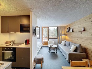 A compact living space with a kitchenette, a sofa, a dining table, and a small stool. - 2-room apartment, slope access, 4 pax, Les Menuires (Les Menuires)