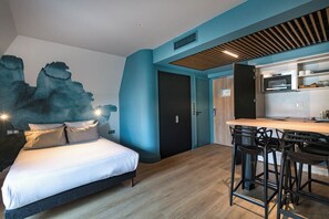 A modern bedroom with a bed, a kitchen area with a counter and stools, and a door leading to another room. - Appartements de la Cité - Saint Malo (Saint-Malo)