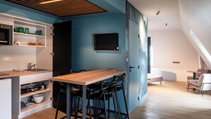 A modern kitchen with white cabinets, a wooden dining table, and black chairs. There is a blackboard on the wall and a TV mounted above it.